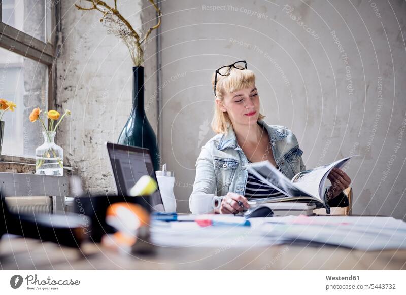 Portrait of smiling woman sitting at desk in a loft leafing through book freelancer freelancing lofts females women Adults grown-ups grownups adult people