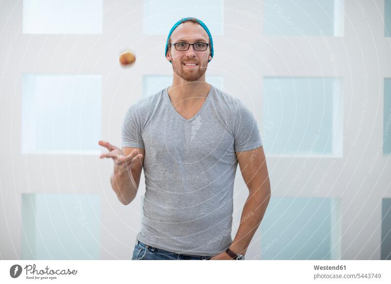 Young man with beanie throwing and apple in the air Apple Apples Office Offices young man young men Fruit Fruits Food foods food and drink Nutrition