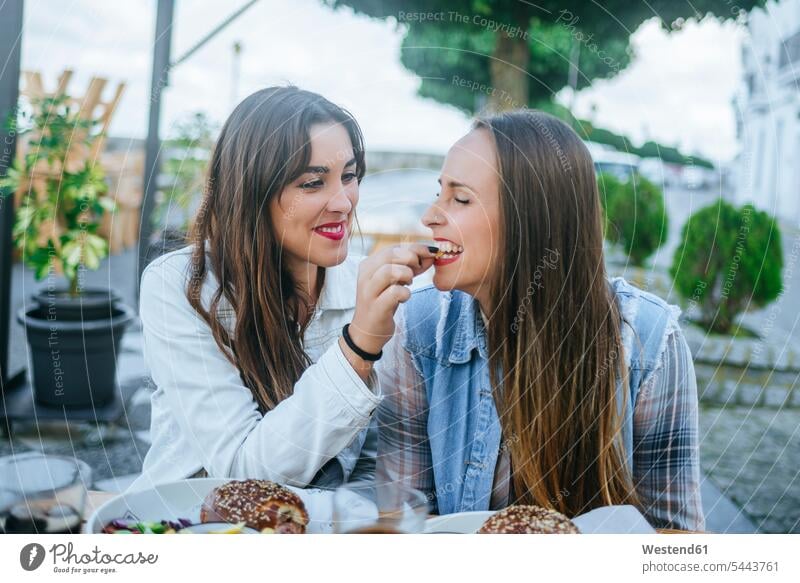 Young woman feeding her friend in a street restaurant eating female friends pavement restaurant sidewalk restaurant Outdoor Restaurant mate friendship