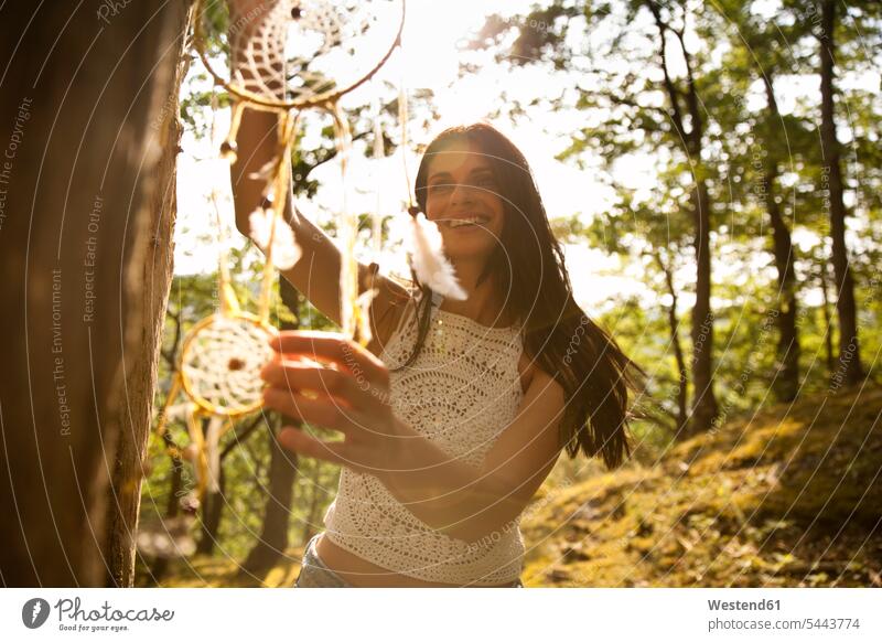 Happy woman hanging dream catcher on a tree dreamcatcher females women smiling smile Tree Trees happiness happy Adults grown-ups grownups adult people persons