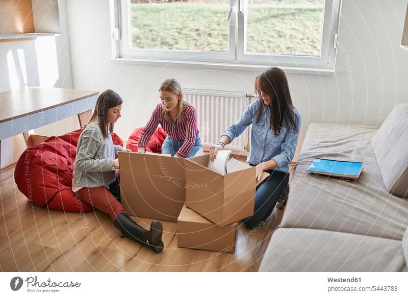 Three young women unpacking cardboard boxes in a room woman females female friends rooms domestic room domestic rooms Cardboard Carton carton Cardboards cartons