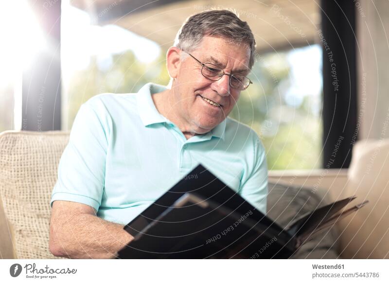 Smiling senior man sitting on couch looking at photo album photograph album photo albums senior men elder man elder men senior citizen smiling smile home