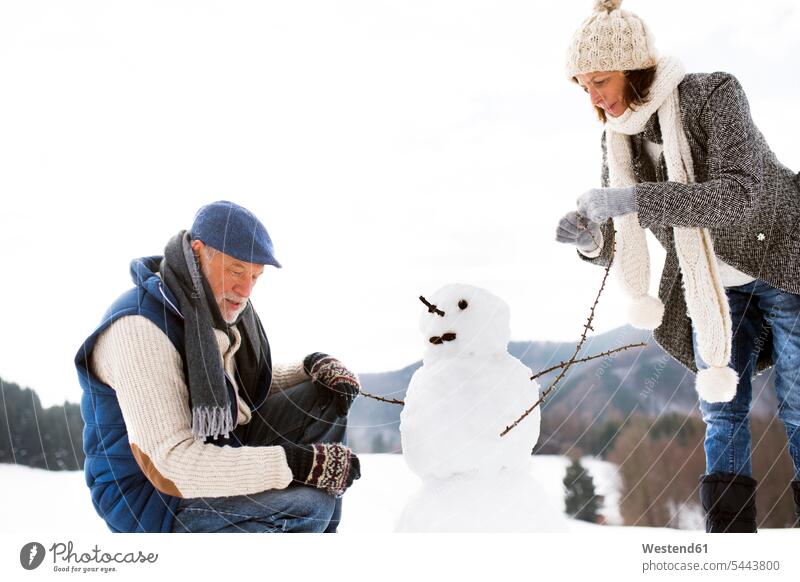 Senior couple building up snowman in winter senior couple elder couples senior couples snowmen twosomes partnership adult couple adult couples people persons