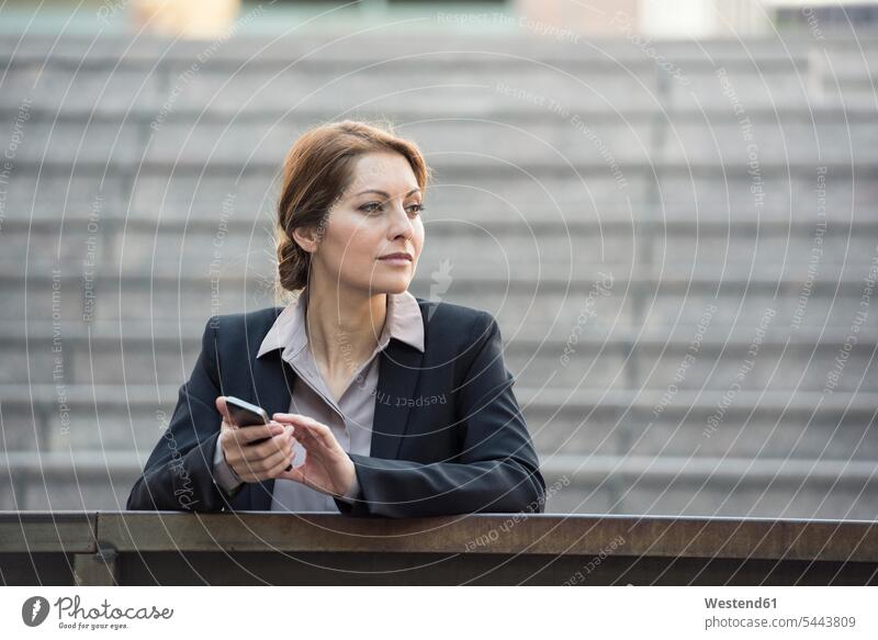 Businesswoman holding cell phone outdoors looking away mobile phone mobiles mobile phones Cellphone cell phones businesswoman businesswomen business woman