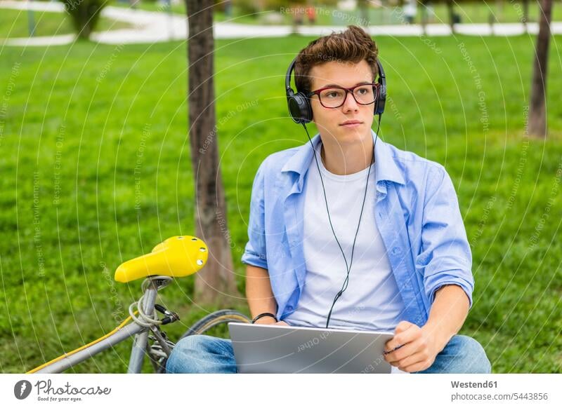 Portrait of serious young man with racing cycle sitting on a bench using laptop and headphones men males headset Laptop Computers laptops notebook Adults