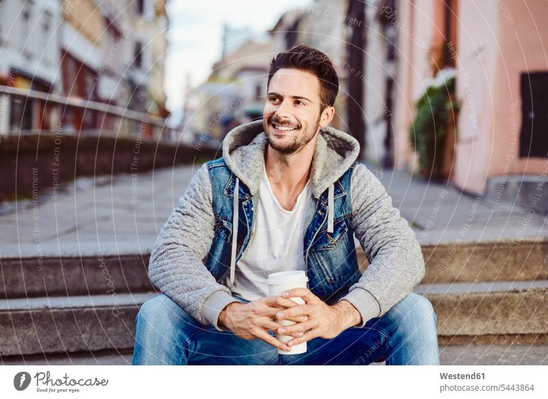 Man with coffee sitting on stairs with city in background happiness happy Seated man men males Coffee smiling smile Adults grown-ups grownups adult people
