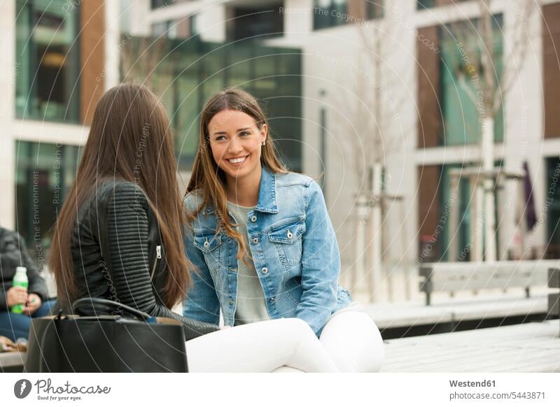 Girlfriends sitting on a bench, chatting meeting encounter gathering Gossip gossiping Chitchat Buzz Seated talking speaking laughing Laughter happiness happy