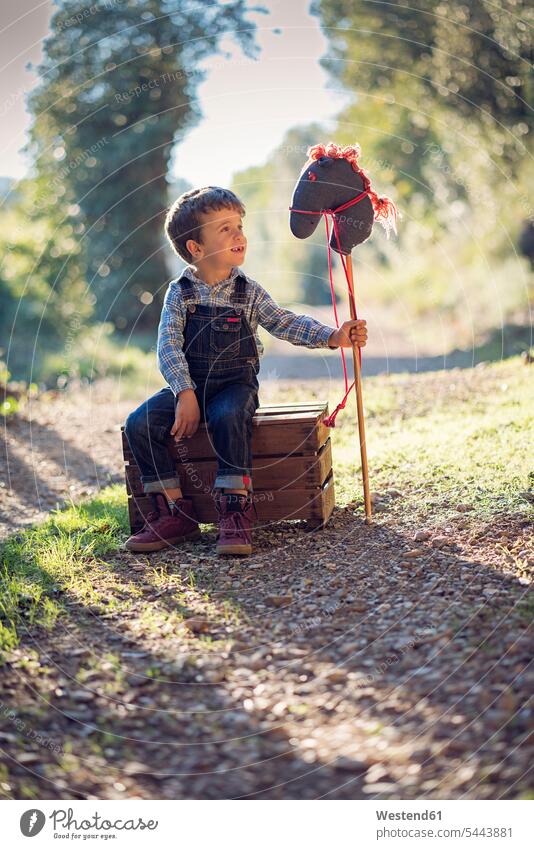 Boy with a hobby horse sitting on wooden box fantasy toy horse childhood toys Seated playing boy boys males children kid kids people persons human being humans