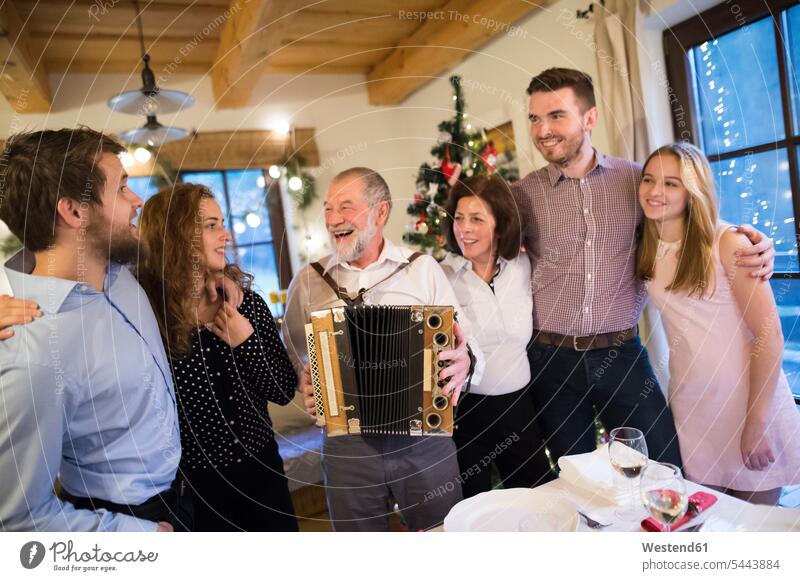 Senior man playing accordion for happy family at Christmas Fun having fun funny X-Mas yule Xmas X mas celebrating celebrate partying Party Parties accordions