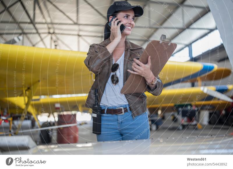 Female pilot talking on the phone in hangar inspecting airplane aeroplanes airplanes call telephoning On The Telephone calling checking Test testing Check