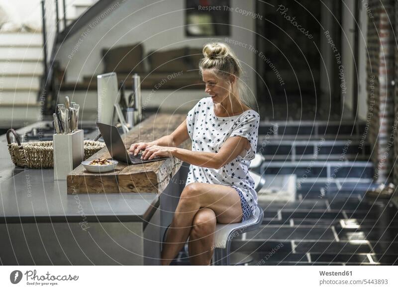 Woman sitting in kitchen, using laptop Laptop Computers laptops notebook woman females women home at home morning in the morning working At Work Seated computer