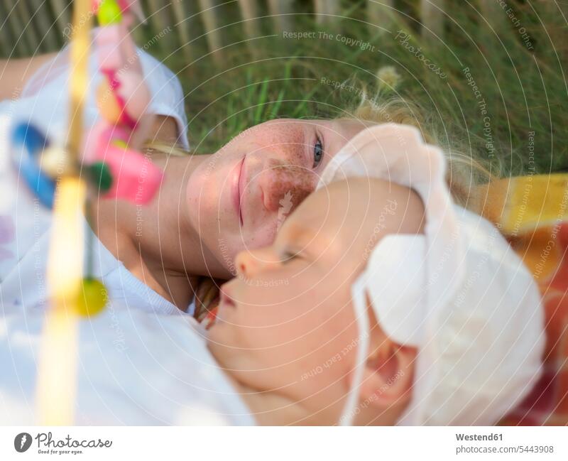 Smiling girl lying with baby girl on blanket on a meadow baby girls female babies infants people persons human being humans human beings sister sisters smiling
