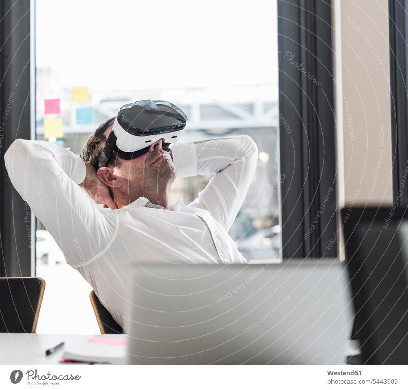Businessman with VR glasses leaning back at desk in office Business man Businessmen Business men offices office room office rooms business people businesspeople