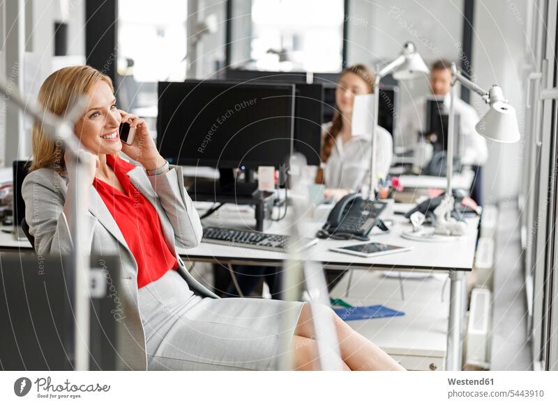 Businesswoman at desk in office on cell phone on the phone call telephoning On The Telephone calling businesswoman businesswomen business woman business women