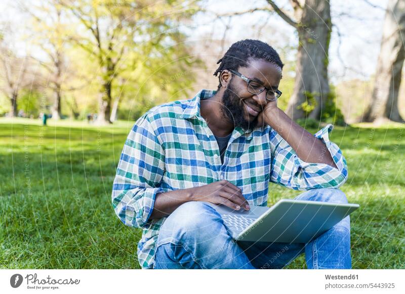 Content man sitting on a meadow using laptop Laptop Computers laptops notebook men males computer computers Adults grown-ups grownups adult people persons
