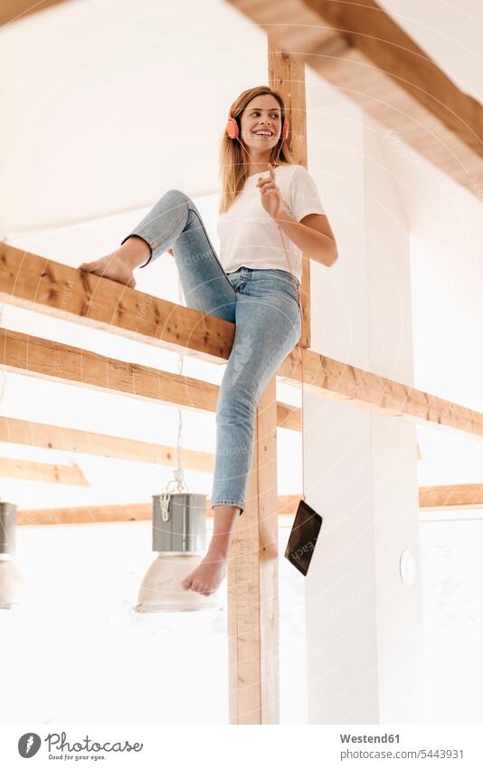 Carefree young woman sitting on ceiling joist, listening music home at home ceiling joists females women tablet digitizer Tablet Computer Tablet PC