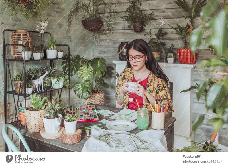 Young woan drinking tea and lookig at her paintings of plants Tea Teas young women young woman aquarelle Watercolor Painting Cactus Cactaceae Cacti Cactuses