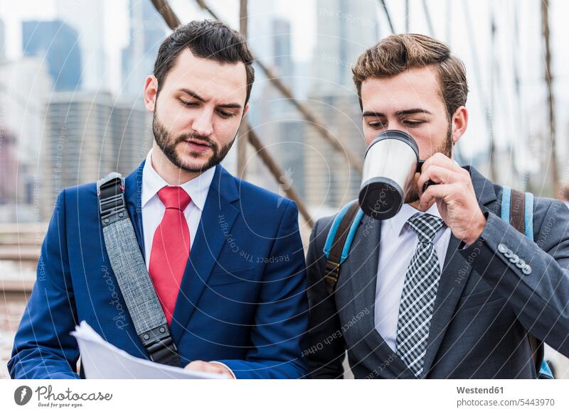 USA, New York City, two businessmen discussing document on Brooklyn Bridge Businessman Business man Businessmen Business men New York State Coffee talking