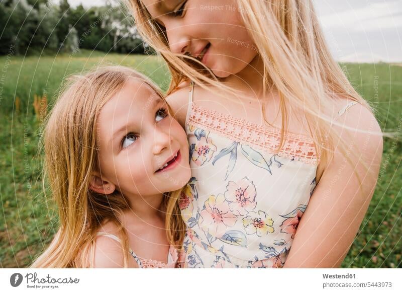 Two little sisters cuddling on a meadow girl females girls portrait portraits child children kid kids people persons human being humans human beings siblings