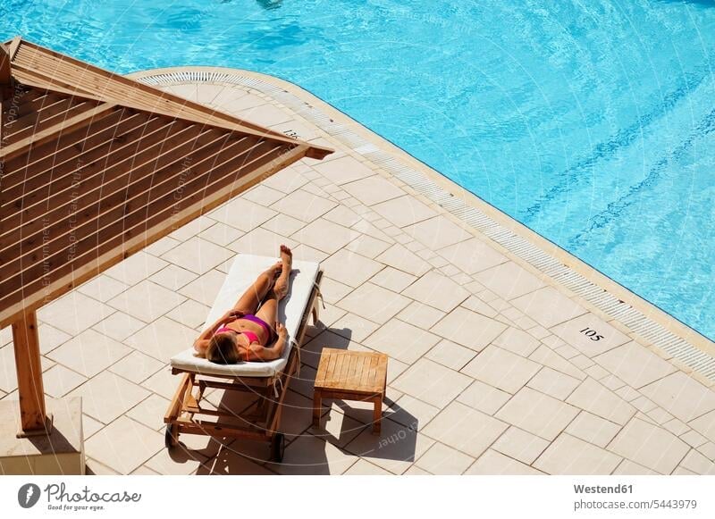 Woman relaxing in sun lounger at the poolside deckchair deck chair deckchairs deck chairs woman females women relaxed relaxation swimming pool swimming pools