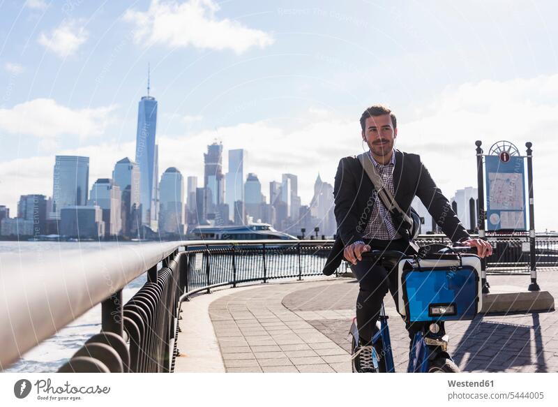 USA, man on bicycle at New Jersey waterfront with view to Manhattan Businessman Business man Businessmen Business men driving drive New York State bikes