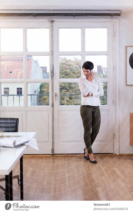 Woman standing at the window in office talking on phone offices office room office rooms businesswoman businesswomen business woman business women females