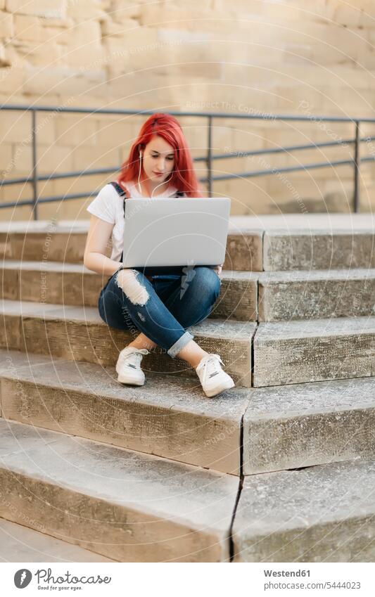 Redheaded woman sitting on stairs using laptop and earphones Laptop Computers laptops notebook females women computer computers Adults grown-ups grownups adult