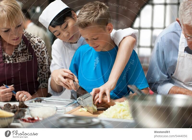 Female chef instructing boy in cooking class female cook kitchen chopping group of people Group groups of people cooks Chefs persons human being humans