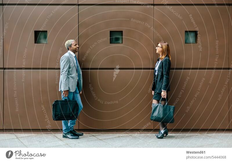 Young businessman and woman standing in front of steel wall, talking business people businesspeople speaking colleagues flirting Flirtation business world