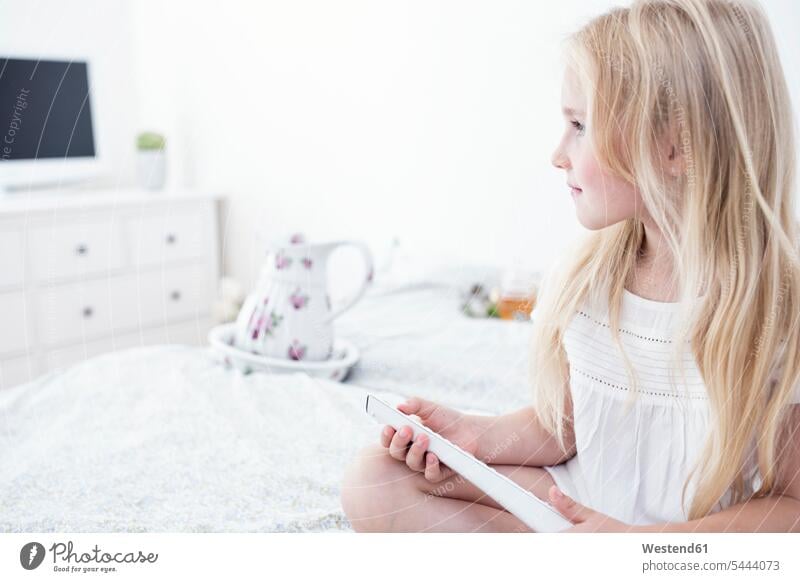 Girl sitting on bed using remote control girl females girls beds Seated child children kid kids people persons human being humans human beings home at home