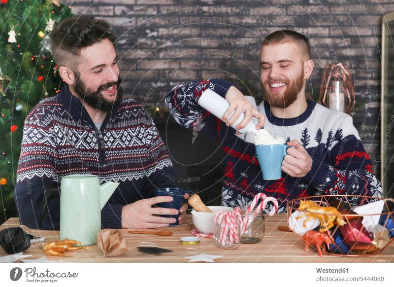 Gay couple preparing hot chocolate with cream and chopped candy canes at Christmas time X-Mas yule Xmas X mas Gay Couple Gays celebration Red-Letter Day