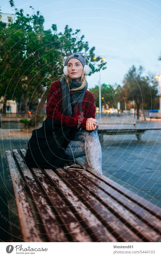Young woman sitting on a bench listening to music females women headphones headset hearing Seated benches Adults grown-ups grownups adult people persons
