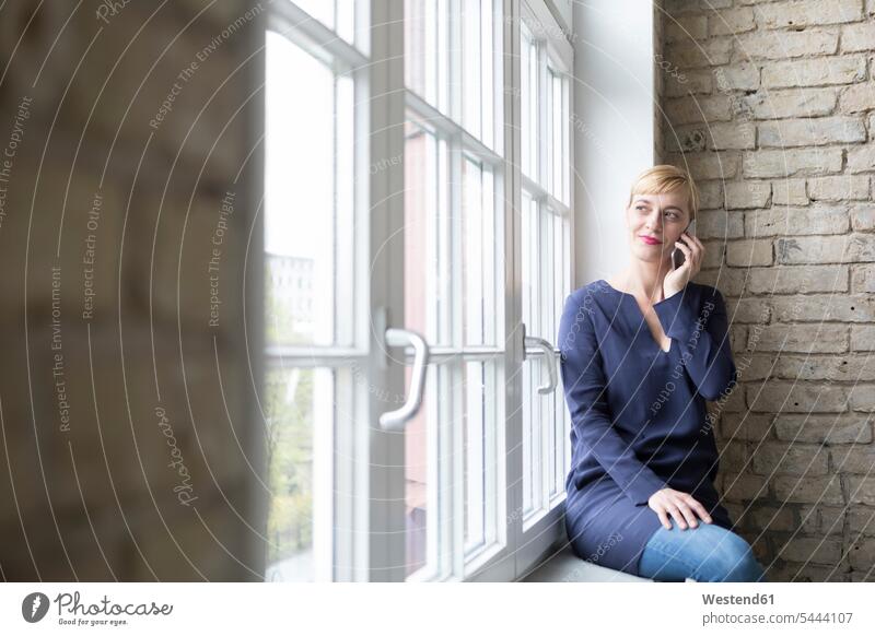 Businesswoman sitting on window sill, making a call Smartphone iPhone Smartphones on the phone telephoning On The Telephone calling windowsill sills