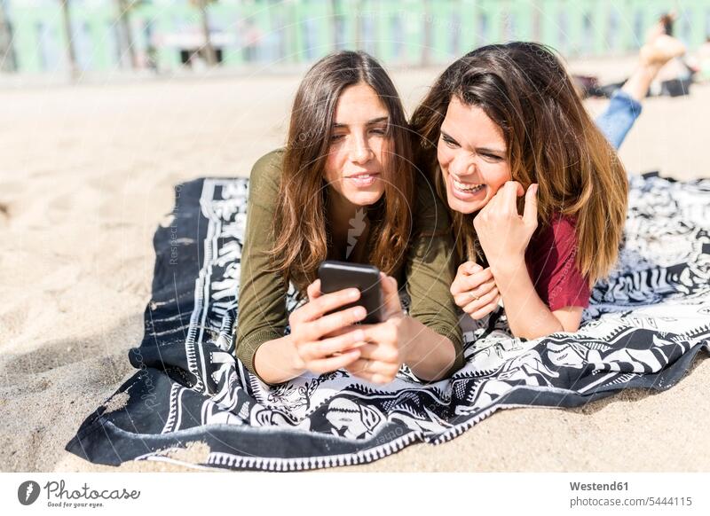 Two happy female friends using cell phone on the beach mobile phone mobiles mobile phones Cellphone cell phones Fun having fun funny beaches mate friendship