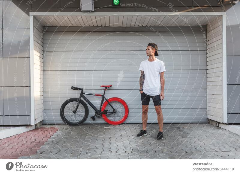 Young man with fixie bike at a roller shutter standing bicycle bikes bicycles men males Adults grown-ups grownups adult people persons human being humans