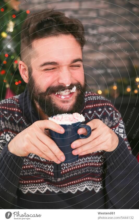 Portrait of laughing man drinking hot chocolate with whipped cream and chopped candy canes portrait portraits Laughter men males positive Emotion Feeling