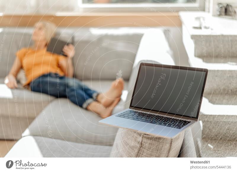 Laptop on couch with woman in background living room living rooms livingroom laptop Laptop Computers laptops notebook settee sofa sofas couches settees females