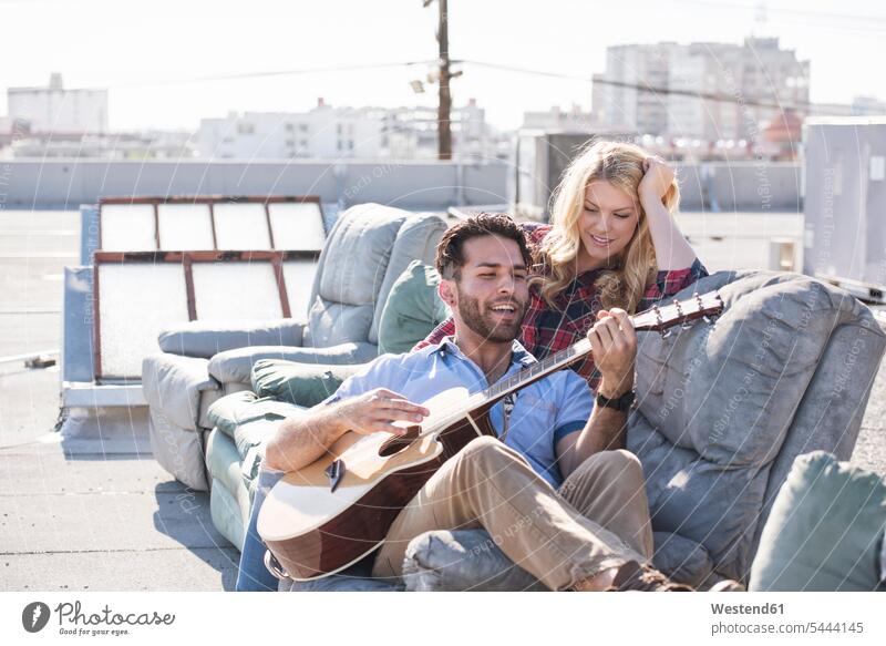 Couple on rooptop sitting on sofa and playing guitar singing musician musicians cheerful gaiety Joyous glad Cheerfulness exhilaration merry gay Seated guitars