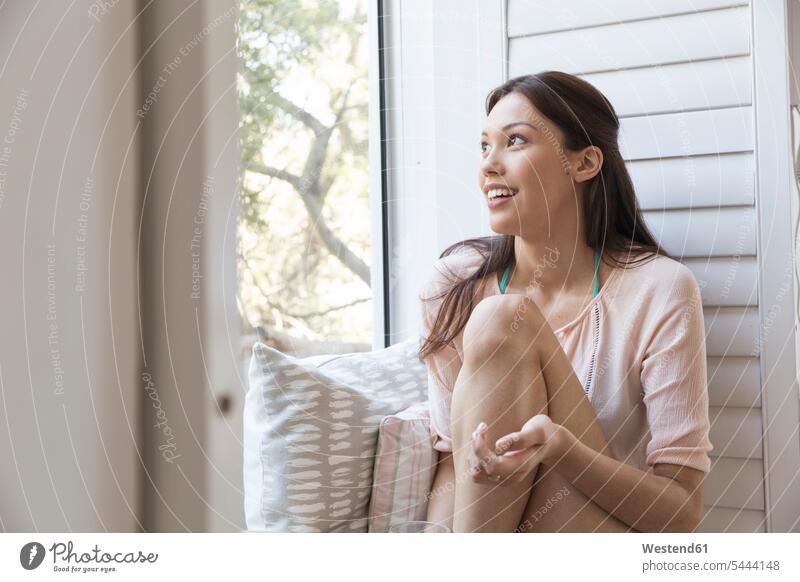 Smiling young woman sitting on windowsill relaxed relaxation Seated females women smiling smile relaxing Adults grown-ups grownups adult people persons