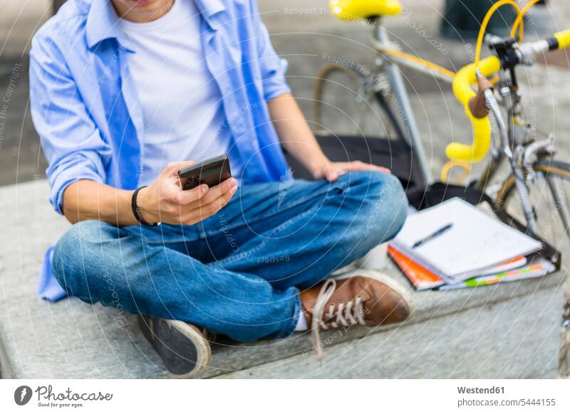 Young man with racing cycle sitting on bench using cell phone Smartphone iPhone Smartphones hand human hand hands human hands mobile phone mobiles mobile phones