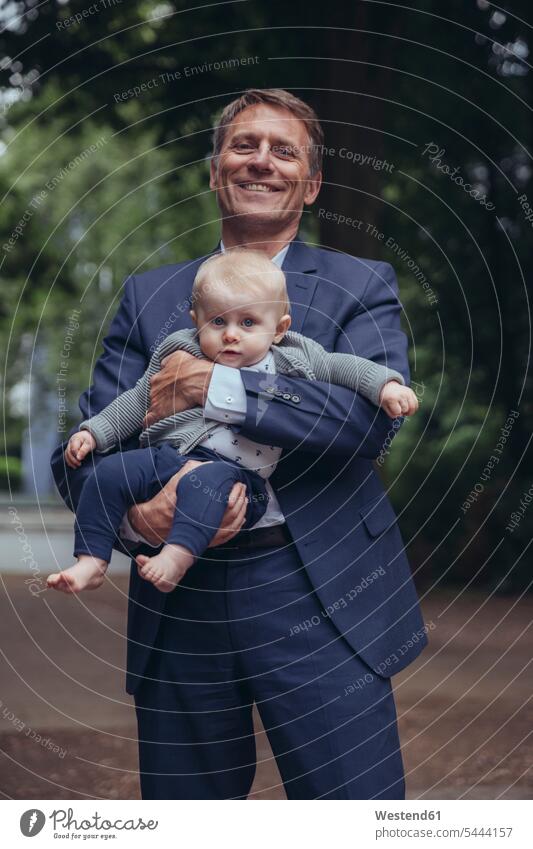 Portrait of smiling mature businessman holding baby boy outdoors smile infants nurselings babies father pa fathers daddy dads papa Businessman Business man