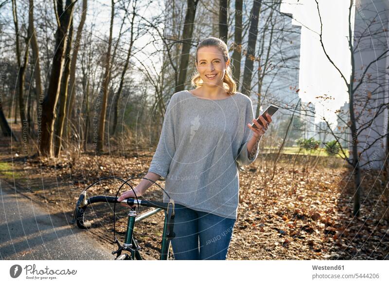 Portrait of smiling blond woman with racing cycle and cell phone portrait portraits females women Adults grown-ups grownups adult people persons human being