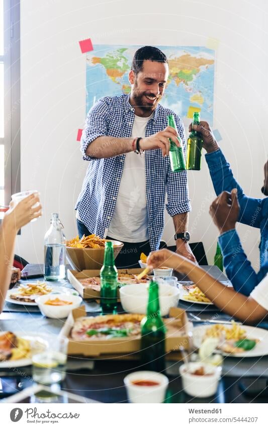 Group of friends clinking beer bottles at dining table Beer Beers Ale Pizza Pizzas eating toasting cheers Table Tables drinking Alcohol alcoholic beverage