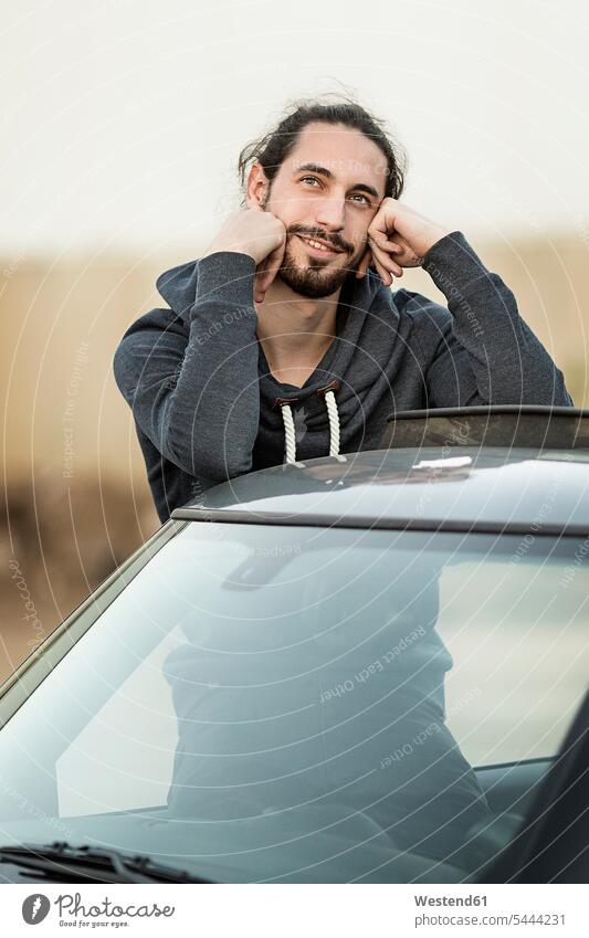 Portrait of daydreaming young man leaning on roof of his car men males portrait portraits automobile Auto cars motorcars Automobiles Adults grown-ups grownups