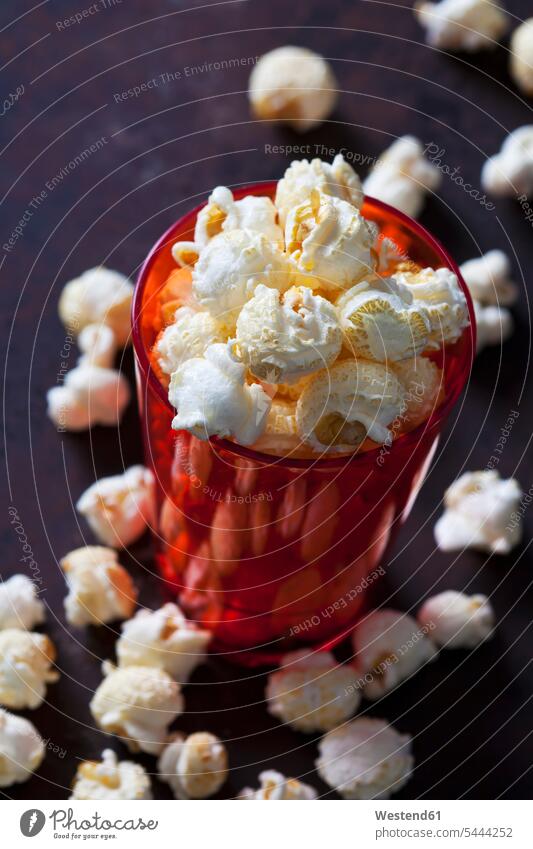 Red plastic cup of popcorn synthetics gleaming prepared munchies nibbles maize ready to eat ready-to-eat scattered dark background sweet Sugary sweets