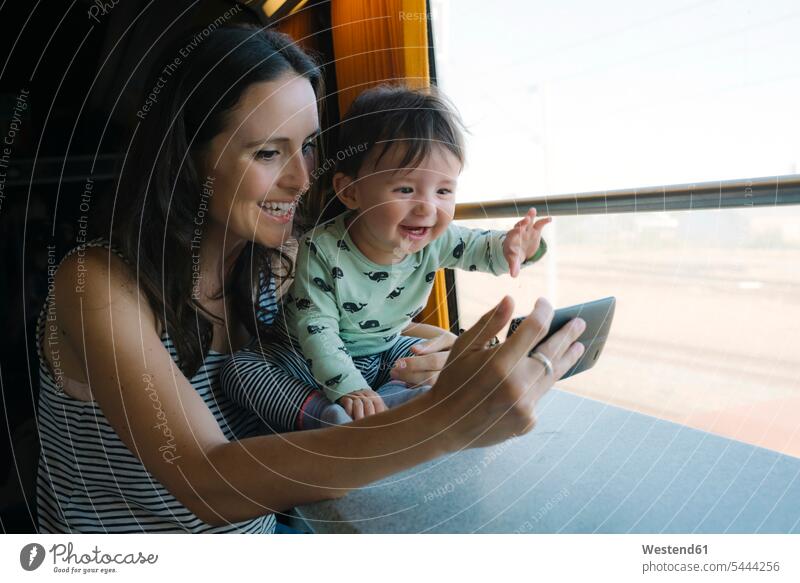 Happy mother and baby girl using smartphone while traveling by train mommy mothers mummy mama travelling mobile phone mobiles mobile phones Cellphone cell phone