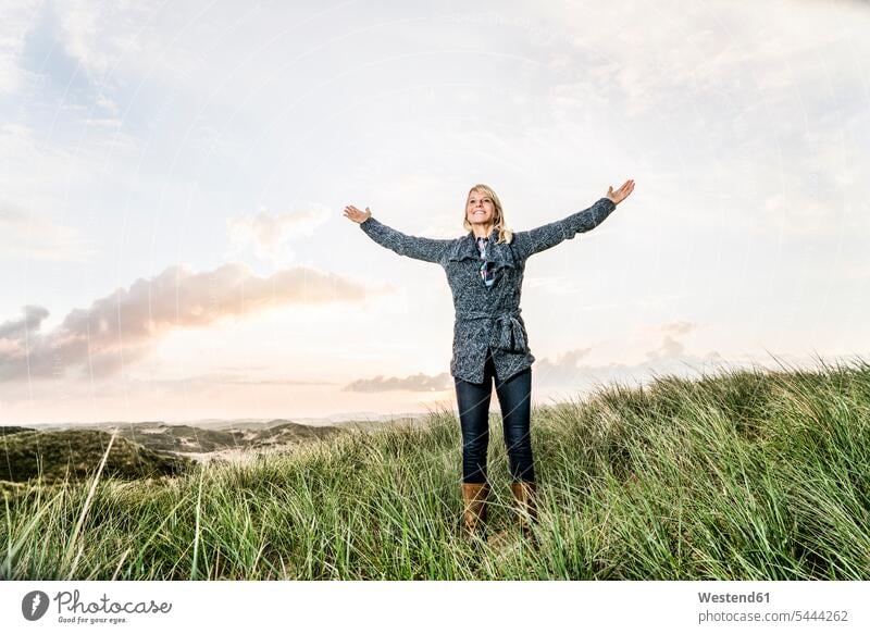 Happy woman standing in dunes with raised arms sand dune sand dunes smiling smile beach beaches females women Adults grown-ups grownups adult people persons