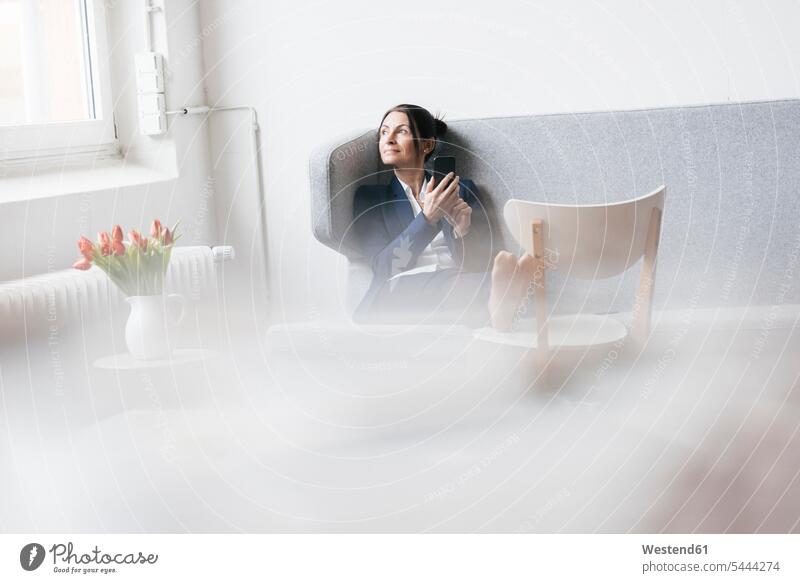 Businesswoman sitting on couch in a loft looking out of the window females women businesswoman businesswomen business woman business women Adults grown-ups