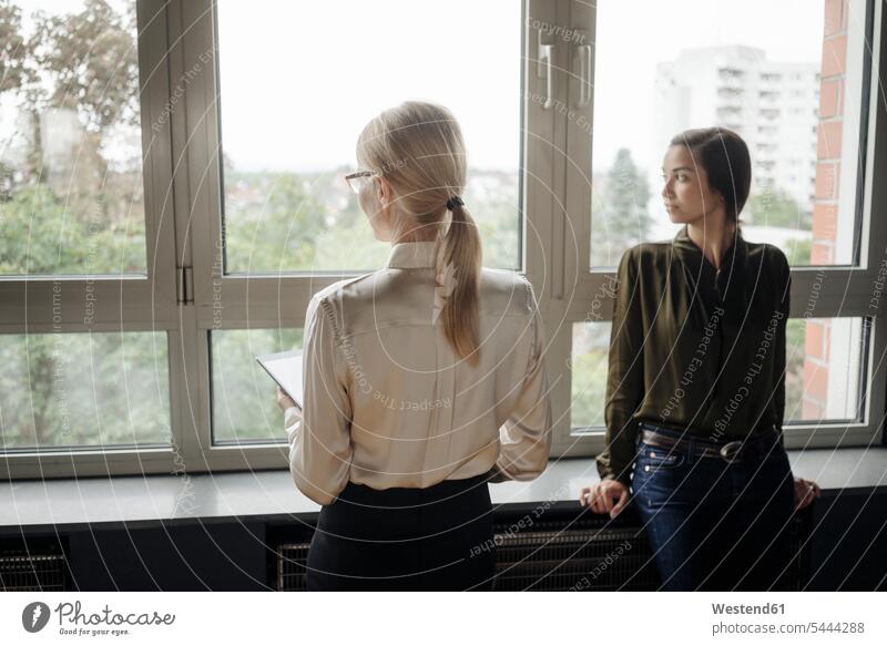 Two businesswomen in office looking out of window businesswoman business woman business women view seeing viewing windows business people businesspeople