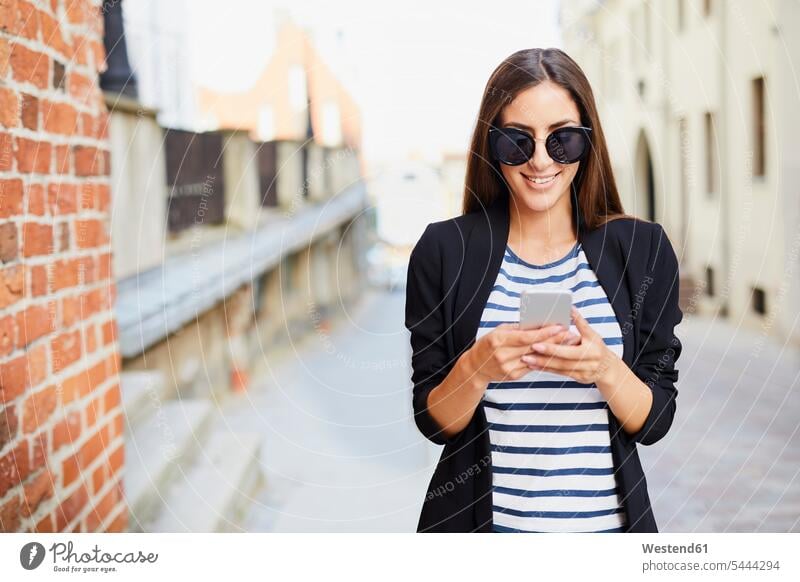 Young woman wearing sunglasses using phone outdoors mobile phone mobiles mobile phones Cellphone cell phone cell phones smiling smile females women telephones